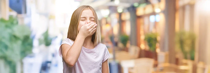 Young girl covering her mouth due to bad breath, illustrating pediatric dental care for children. Young girl covering her mouth due to bad breath, illustrating pediatric dental care for children.