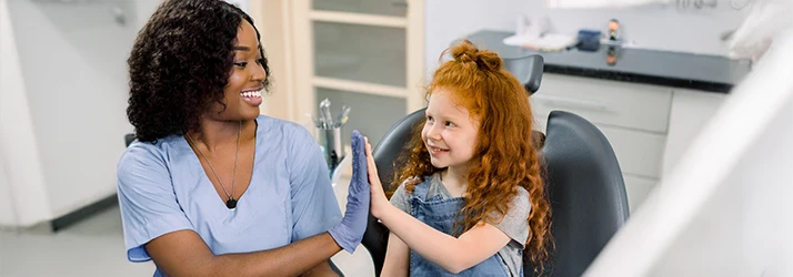 Pediatric dentist giving a cheerful high-five to a young girl, celebrating cavity prevention success. Pediatric dentist giving a cheerful high-five to a young girl, celebrating cavity prevention success.