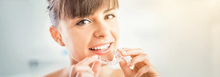 Teen girl smiling while holding clear orthodontic aligner. Teen girl smiling while holding clear orthodontic aligner.