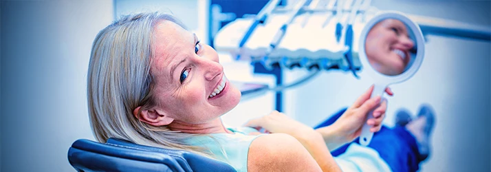A middle aged woman with smile lines and silver tinsled hair grins over shoulder from the exam chair A middle aged woman with smile lines and silver tinsled hair grins over shoulder from the exam chair