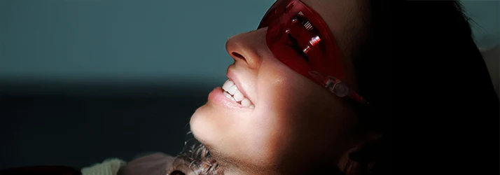 A patient wearing red protective eyewear bares teeth into a shining light A patient wearing red protective eyewear bares teeth into a shining light