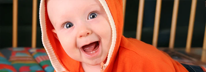 A wide eyed baby in an orange hood gapes happily at the camera showing off two tiny bottom teeth A wide eyed baby in an orange hood gapes happily at the camera showing off two tiny bottom teeth