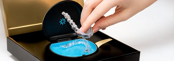 A hand gently holding an invisalign set returns it to its small case where another invisalign for the second row of teeth sits A hand gently holding an invisalign set returns it to its small case where another invisalign for the second row of teeth sits