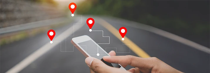 A hand holds a cellphone with the open road in the background with an interactive location map displaying from the phone A hand holds a cellphone with the open road in the background with an interactive location map displaying from the phone