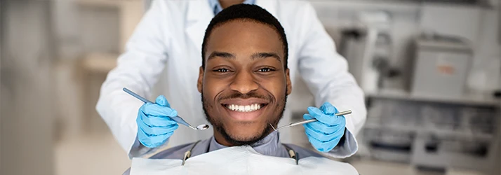 Man with black hair and beard smiles brightly as the dentist reaches around with dental tools to examine the patient's teeth Man with black hair and beard smiles brightly as the dentist reaches around with dental tools to examine the patient's teeth
