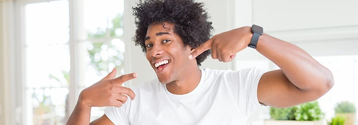 A man with curly hair gestures to his winning smile as bright as his white t-shirt A man with curly hair gestures to his winning smile as bright as his white t-shirt
