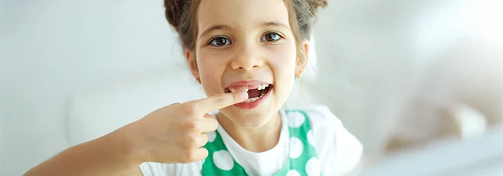 Young girl happily pointing to her missing baby tooth, representing natural tooth loss in childhood. Young girl happily pointing to her missing baby tooth, representing natural tooth loss in childhood.