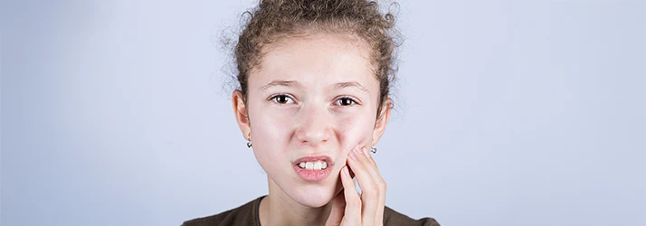 Girl holding cheek in discomfort after biting it due to dental anesthesia, highlighting pediatric dental aftercare. Girl holding cheek in discomfort after biting it due to dental anesthesia, highlighting pediatric dental aftercare.