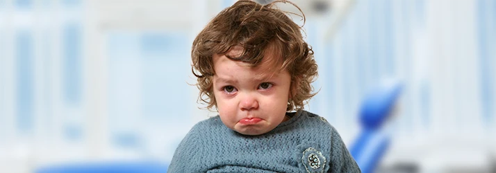 Young child looking anxious and upset at the dental office, highlighting pediatric dental anxiety management. Young child looking anxious and upset at the dental office, highlighting pediatric dental anxiety management.
