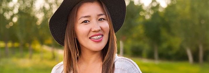 Smiling adult woman wearing a hat outdoors, confidently showing her orthodontic braces. Smiling adult woman wearing a hat outdoors, confidently showing her orthodontic braces.