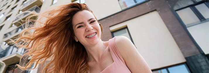 Joyful adult woman with flowing hair smiling confidently outdoors, showing her orthodontic braces.