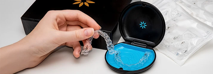 Hand holding a clear Invisalign aligner next to its open storage case, showcasing orthodontic aligner treatment.