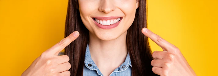 Smiling woman pointing at her straight, white teeth after successful orthodontic teeth straightening treatment.