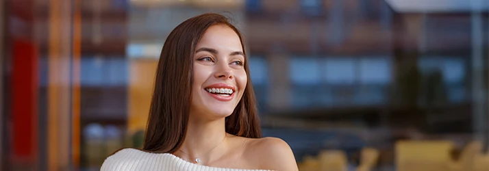 Young woman smiling confidently outdoors, showcasing her metal orthodontic braces. Young woman smiling confidently outdoors, showcasing her metal orthodontic braces.