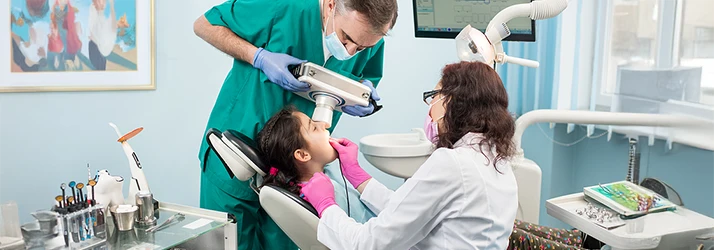 Pediatric dental team providing emergency dental care to a child patient using advanced dental equipment.