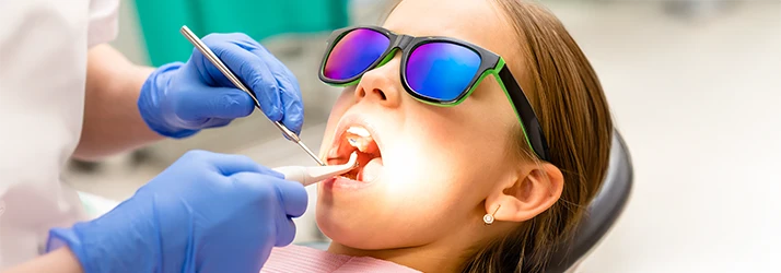 Child wearing protective glasses receiving dental filling treatment at pediatric dental office. Child wearing protective glasses receiving dental filling treatment at pediatric dental office.