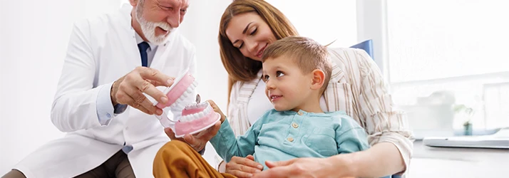 Pediatric dentist explaining post-tooth extraction care to a child and mother using a dental model. Pediatric dentist explaining post-tooth extraction care to a child and mother using a dental model.