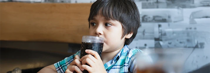 Young boy drinking sugary soda, emphasizing risks of tooth discoloration and pediatric dental care. Young boy drinking sugary soda, emphasizing risks of tooth discoloration and pediatric dental care.
