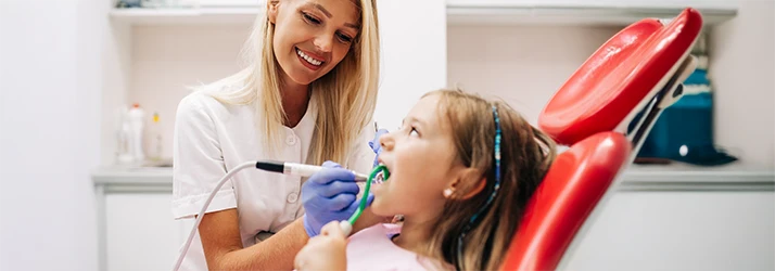 Pediatric dentist performing professional teeth cleaning on a young girl, promoting healthy oral hygiene. Pediatric dentist performing professional teeth cleaning on a young girl, promoting healthy oral hygiene.