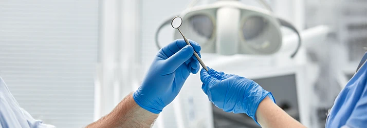 Oral surgeon and assistant handing dental instruments during precise oral surgery procedure.