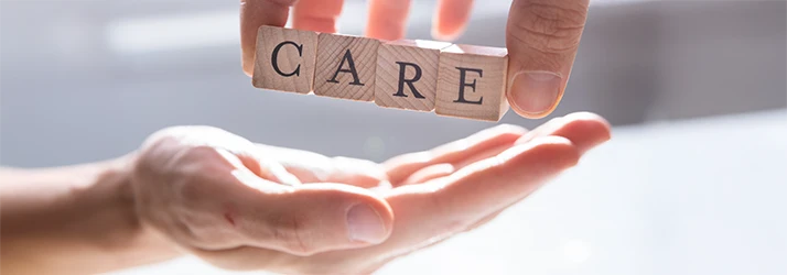 Hand placing wooden blocks spelling 'CARE' into another open hand, symbolizing compassionate patient care in oral surgery.