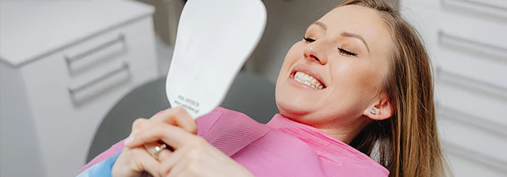 Woman checking out her dental implants in a mirror from a periodontist.