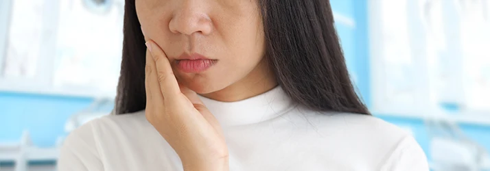 Woman experiencing discomfort due to gingivitis, holding her cheek in pain, needing gingivitis treatment from a periodontist.