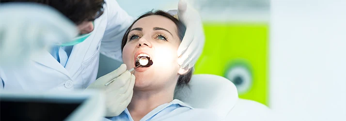 Periodontist examining a female patient's teeth and gums with a dental mirror during a periodontal checkup. Periodontist examining a female patient's teeth and gums with a dental mirror during a periodontal checkup.