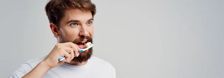 Man-Brushing-His-Teeth-In-Front-Of-Grey-Background.webp