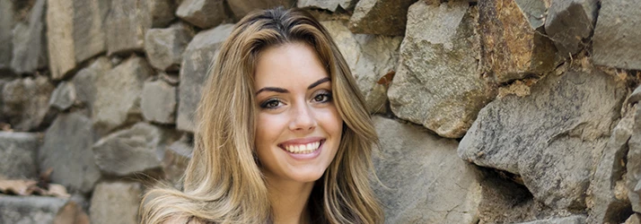 Woman-Smiling-In-Front-Of-A-Flagstone-Wall.webp