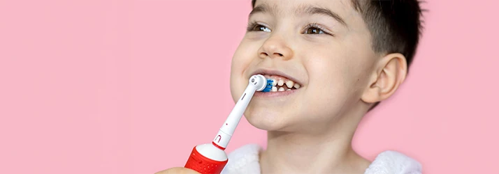 Young-Child-Brushing-His-Teeth-In-Front-Of-Pink-Background.webp